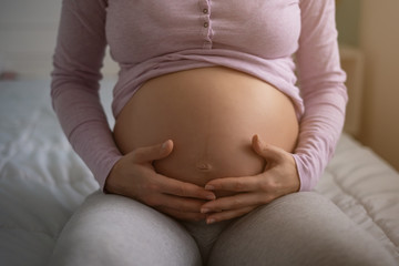 Pregnant woman holding her stomach and relaxing at home.