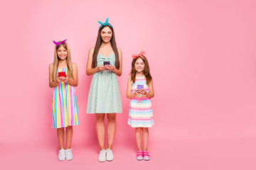 Full size photo of cute woman and two schoolkids having blonde brunette haircut use device wear dress skirt headbands isolated over pink background