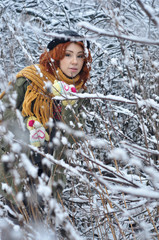 Red-haired cheerful girl warms her hands in warm knitted mittens during a snowfall