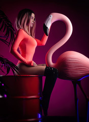 a girl in a bright bodysuit poses with a large Flamingo figurine