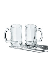 Detailing shot of a pair of classic design beer mugs with thick glass handles. The beer glasses are isolated on the white surface with shadows.  