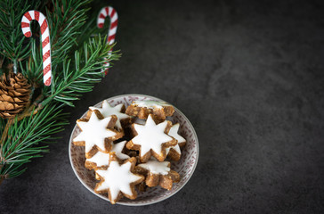 A cup with christmas biscuits and fir branch on a black table and copy space, top view