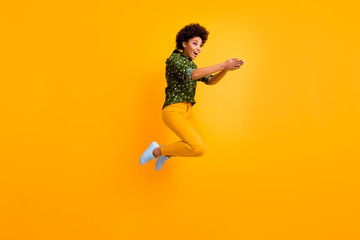 Fototapeta na wymiar Full body photo of crazy dark skin curly lady jumping high making swimming moves excited to start competition wear green dotted shirt trousers isolated yellow color background