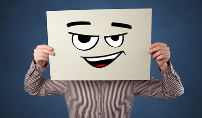 Casual person holding a paper in front of his face with drawn emoticon face