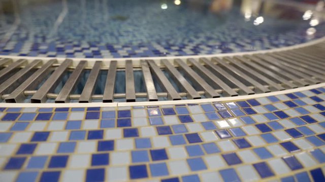 Close up side blue mosaic tiles water drain system in the pool of the water Park Steadicam shooting