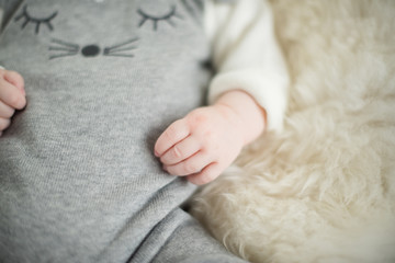 A beautiful soft delicate warm young baby hand photographed with a shallow depth of field. gentle calm colours and feel. baby care and well being. babies hands on a cream fur rug.