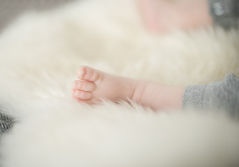 A beautiful soft delicate warm young baby foot photographed with a shallow depth of field. gentle calm colours and feel. baby care and well being. babies feet on a cream fur rug.