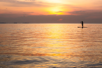 Silhouette of family playing the stand-up paddle board on the sea with beautiful summer sunset colors. Happy family concept.