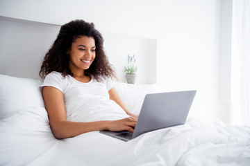 Photo of charming curly dark skin lady lying linen bed covered white blanket hold notebook writing corporate report working weekend saturday morning wear pajama room indoors