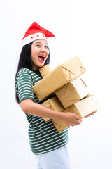 portrait of a young Asian woman wearing a santa hat and wearing casual clothes lifting a pile of gifts with surprise face