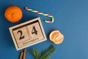 Christmas Eve Date On Calendar with mandarins, cinnamon and fir tree branch on blue trendy background. Festive backdrop for projects. Flat lay style. Top view. Color of the year. December 24