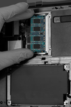 Technician installing RAM into the memory slot on a laptop computer.  Abstract image with selective colour