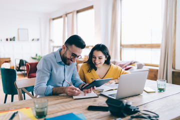 Fototapeta premium Joyful couple taking notes and using gadgets