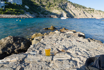 A relaxing Mediterranean sea view, drinking beer on the rocks on a sunny summers evening. Blue waters and rocky mountain views. Drinking alcohol on holiday whilst abroad on vacation.