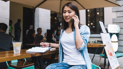 Cheerful Asian woman talking on smartphone and looking at camera