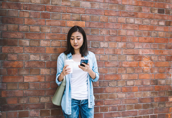 Asian woman standing next to wall with mug of coffee