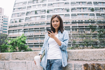 Asian young woman looking at camera while using smartphone