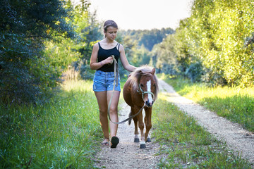 Teenage girl walking with a pony colt on a leash along a country road