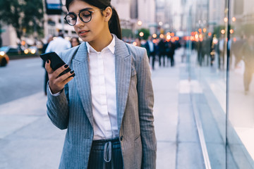 Young formal pretty young businesswoman surfing smartphone on street