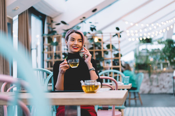 Trendy amused modern woman talking on phone at cafe
