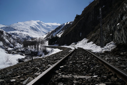 railroad tracks amidst snowcapped mountains against clear sky