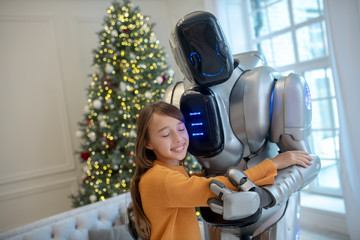 Cute girl in orange shirt hugging her robot friend