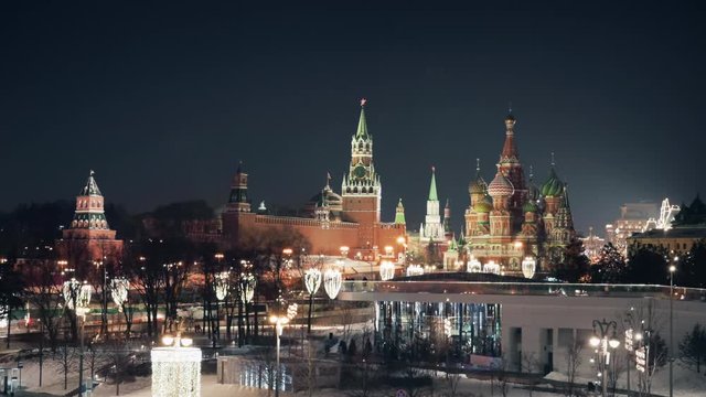 Beautiful panorama of Moscow Red Square on a calm winter night with illuminated Kremlin clock tower and the Cathedral of Vasily the Blessed. Rare cars passing by along the decorated streets.