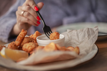 close-up of woman hands holding the fork with nuggets and soaks in a sauce sit in cozy cafe . Female dressed warm woolen sweater and siting on the sofa.
