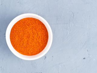 Ground red chili pepper in a white bowl on a gray concrete background. Healthy eating concept
