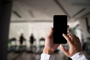 Hand held black phone With a blank white screen in the gym in the morning light.