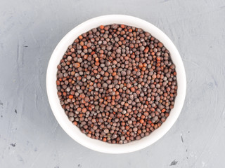 Mustard seeds in a white bowl on a gray concrete background. Healthy eating concept