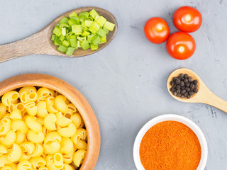 Pasta, small tomatoes, green onion, black pepper, red chili in wooden spoon on a gray concrete background. Healthy eating concept