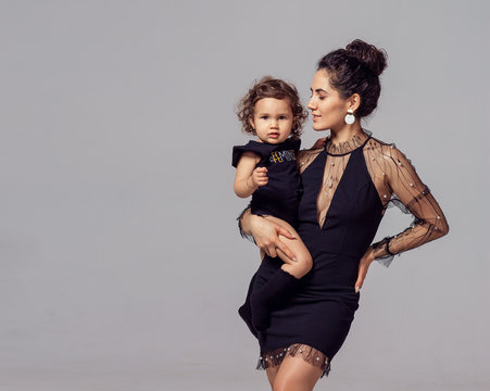fashion mom in black elegant dress and oriental Caucasian kid. studio gray background photo shoot style exquisitely festive feminism. holiday new year mother's day outfit  daughter girl boy son baby