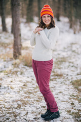 Young woman in an orange cap enjoying the sunny weather outdoors after first snow in the woods.