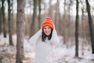 Young woman in an orange cap enjoying the sunny weather outdoors after first snow in the woods.