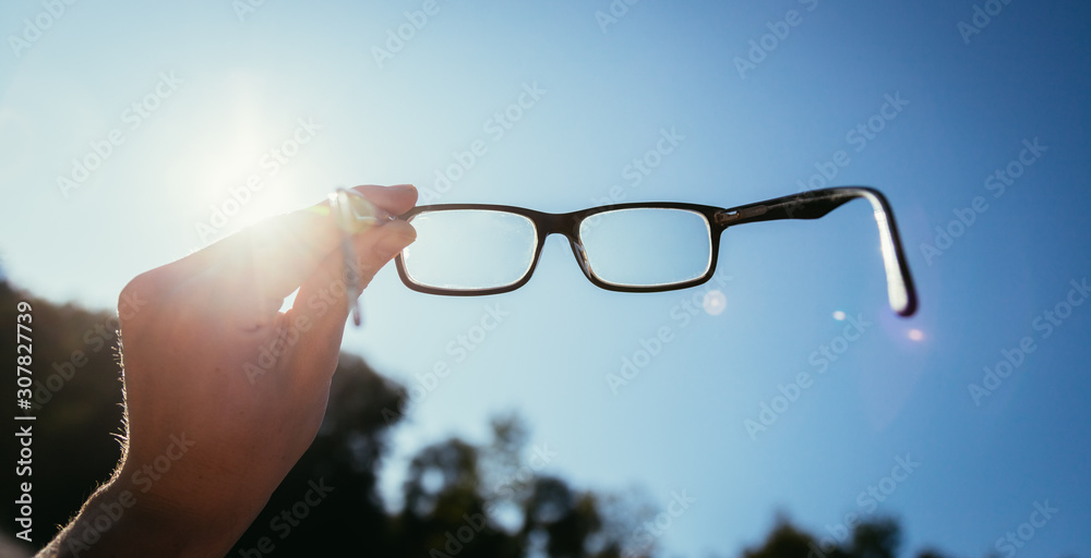 Wall mural Hand holding glasses outdoors, blue sky, sunbeam with lens flares