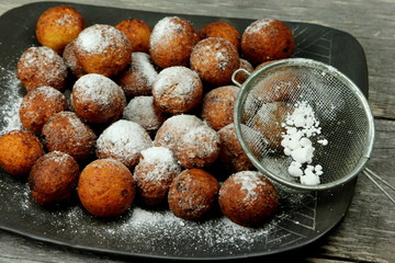 Small balls of freshly baked homemade cottage cheese with sugar powder on black background. Freshly made donuts from cottage cheese with powdered sugar
