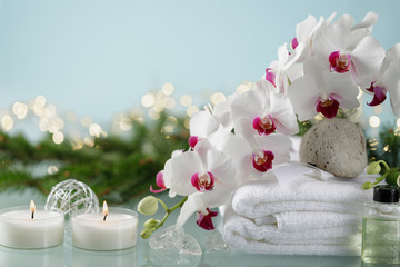 Christmas spa decoration on blue background with an orchid, candles, christmas tree branch and garland lights