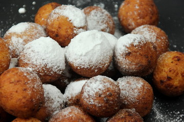 Small balls of freshly baked homemade cottage cheese with sugar powder on black background. Freshly made donuts from cottage cheese with powdered sugar