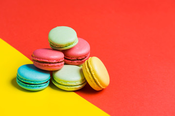Fototapeta na wymiar baked French multicolored macaroons on red and yellow background with copy space