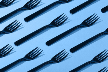 Many black plastic forks on vibrant background. Main color trend for 2020 year.