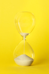 Time is running out concept. An hourglass with sand dripping through, on a vibrant yellow background