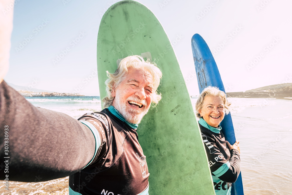 Wall mural happy couple of seniors at the beach trying to go surf and having fun together - mature woman and ma