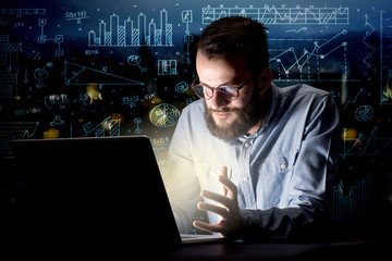 Young handsome businessman working late at night in the office with blue calculations in the background