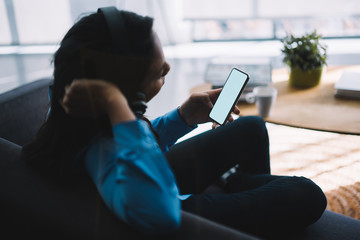 Adult black female surfing smartphone while listening to music at home