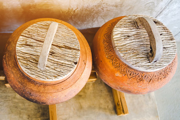 Row of earthen jars with wood lids and rough gray floor for water storage in Asian house. Selective focus on wood lids. © JinnaritT