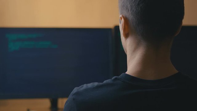 Rear view of IT programmer engineer developer writing programming code on computer monitor