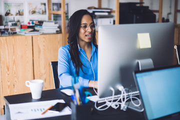 Young African American woman speaking at work place using earphones and computer