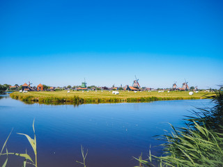 Fototapeta na wymiar Landscape with typical dutch windmill village Zaanse Schans in Zaandam, Netherlands. Traditional dutch windmills located by the river Zaan. Culture museum travel and scenery landscape