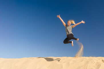 ein Mädchen springt im Sommer voller Lebensfreude von einer Sanddüne und wirbelt dabei Staub auf